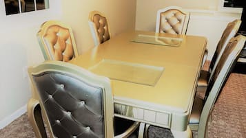 A dining room with a beige table and chairs, carpeted floor, and a window with blinds.