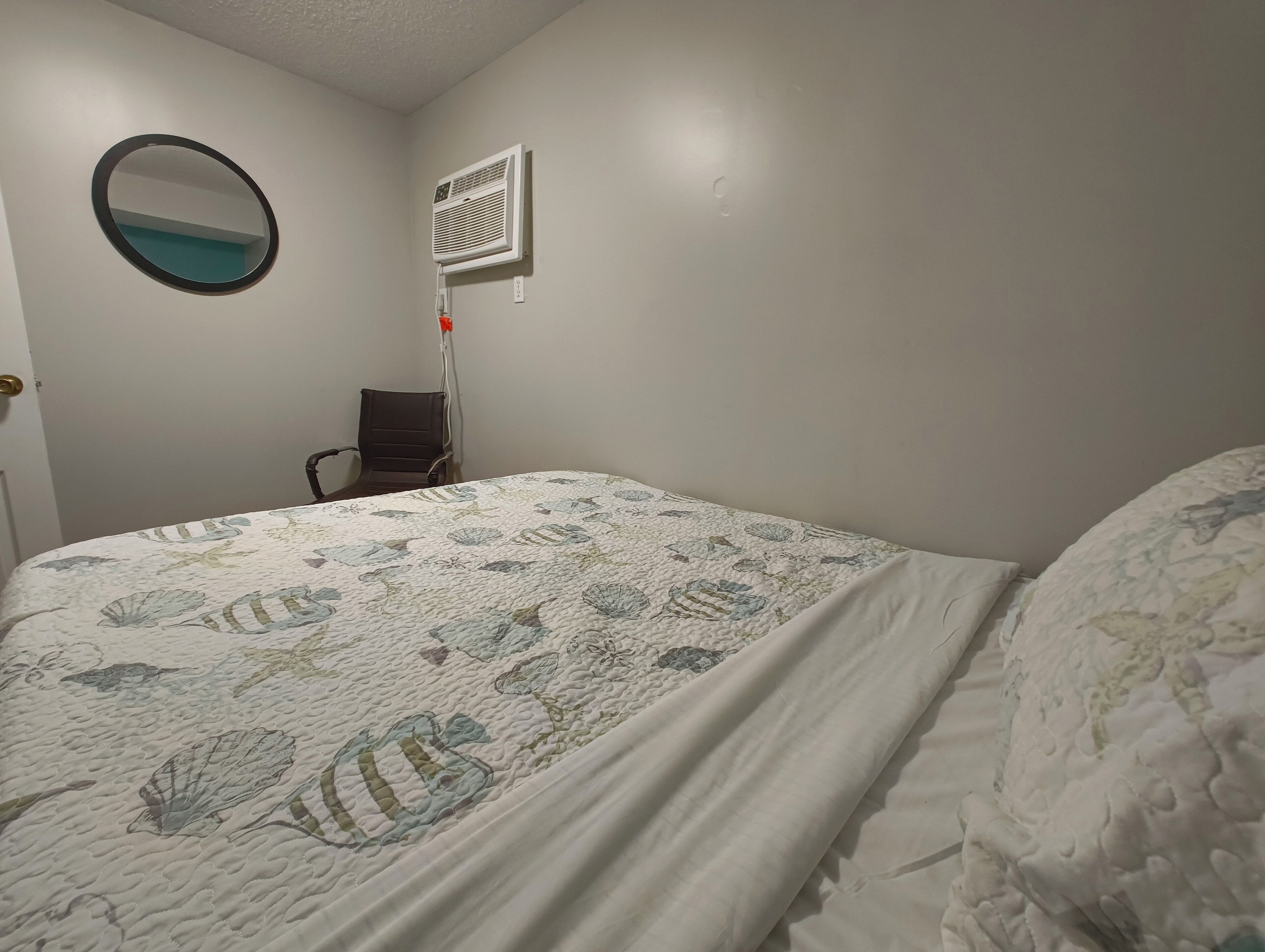 Una camera da letto con un letto, una sedia, un condizionatore d'aria a parete e uno specchio rotondo.