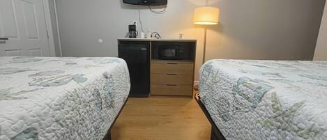 A hotel room with two beds, a TV mounted on the wall, a desk with a microwave, and a lamp.