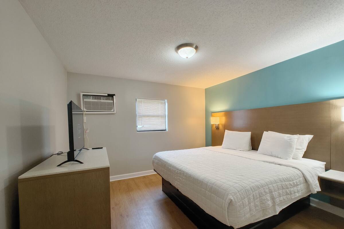 Una habitación de hotel con cama, mesita de noche y escritorio con computadora.