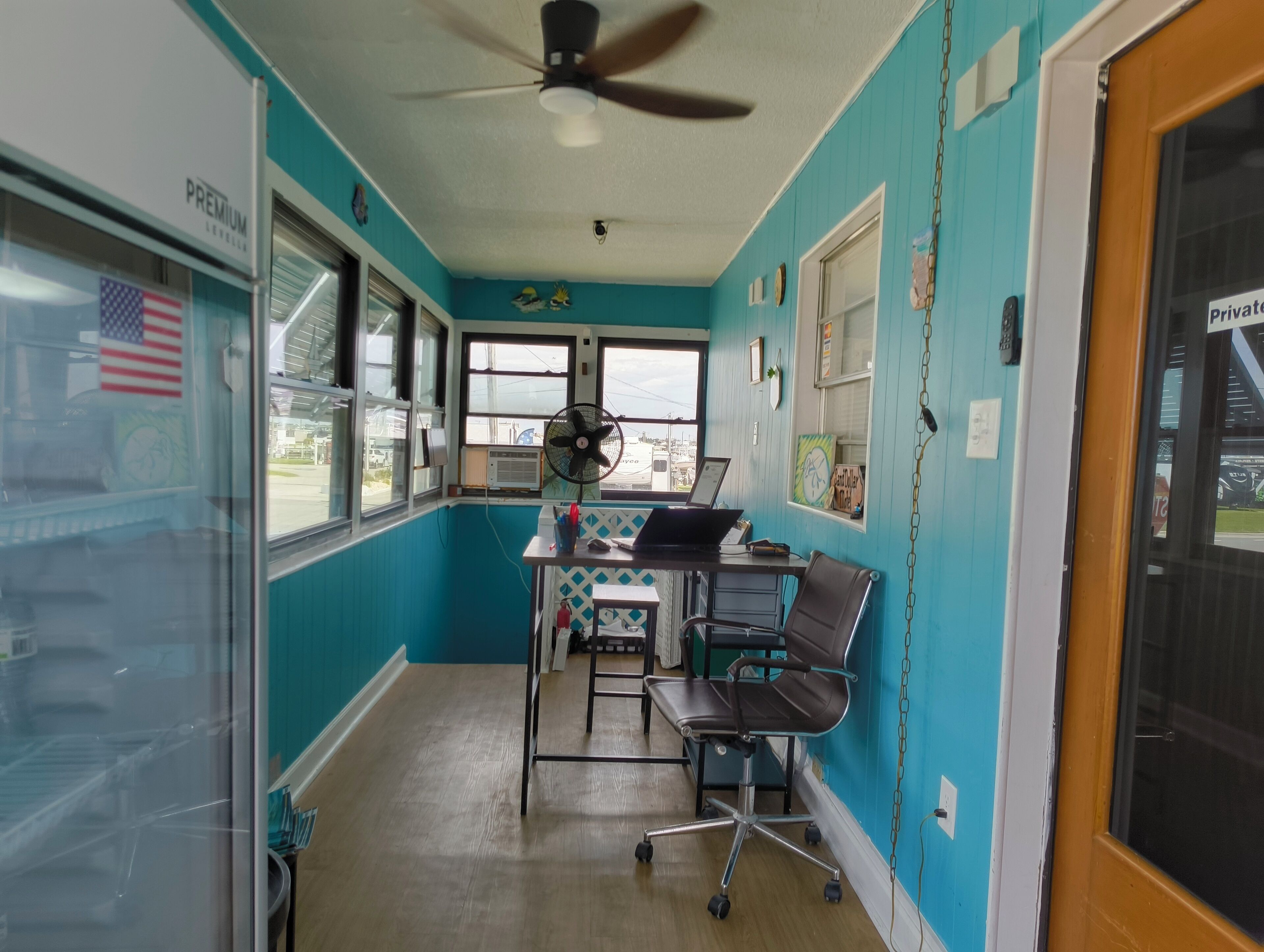 Una habitación con paredes color turquesa, un ventilador de techo, un escritorio con una computadora portátil y una silla.