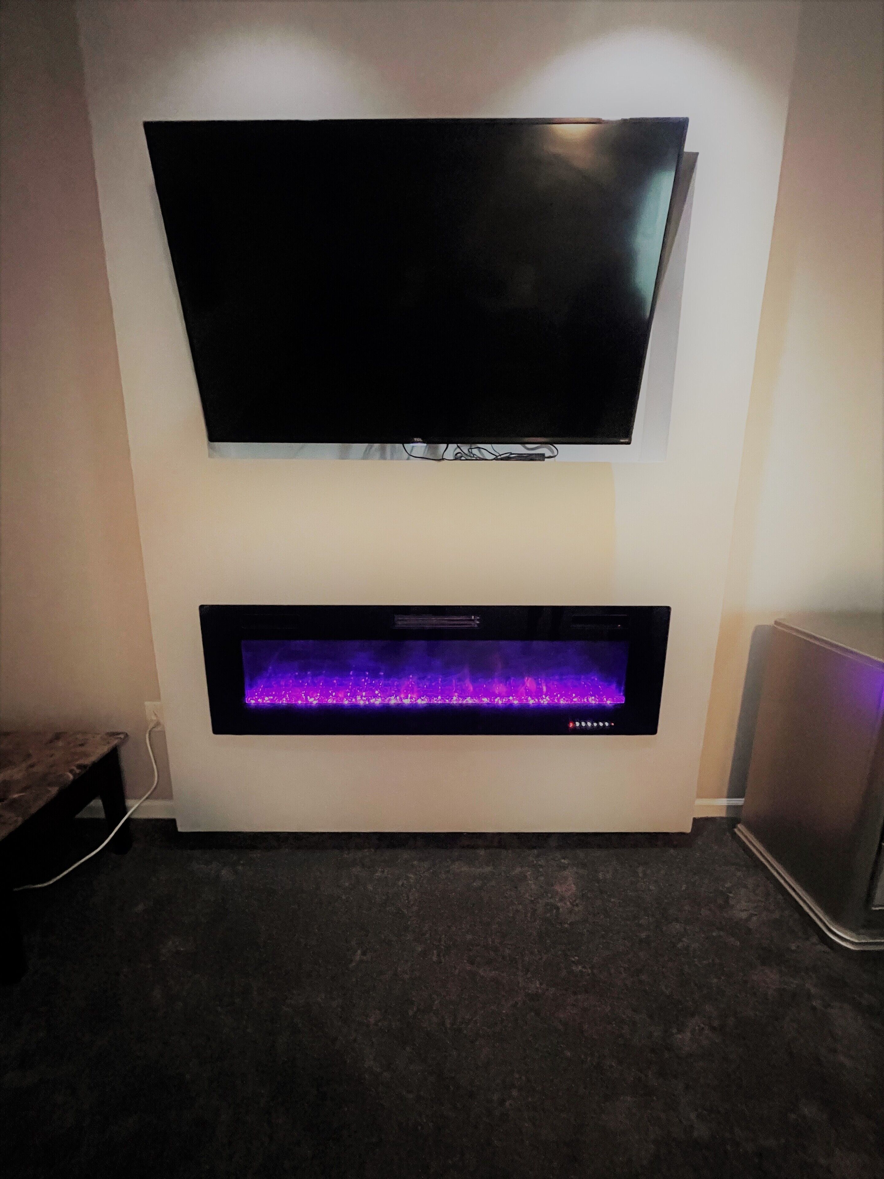 A flat-screen TV mounted above a built-in fireplace with a purple-lit fire.