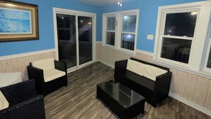 A living room with a blue wall, a ceiling fan, and a large window. - Sand Dollar Motel (Atlantic Beach)