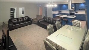 A living room with a dark brown leather sofa, a dining table with chairs, and a kitchen area with blue cabinets and a stainless steel range hood. - Sand Dollar Motel (Atlantic Beach)