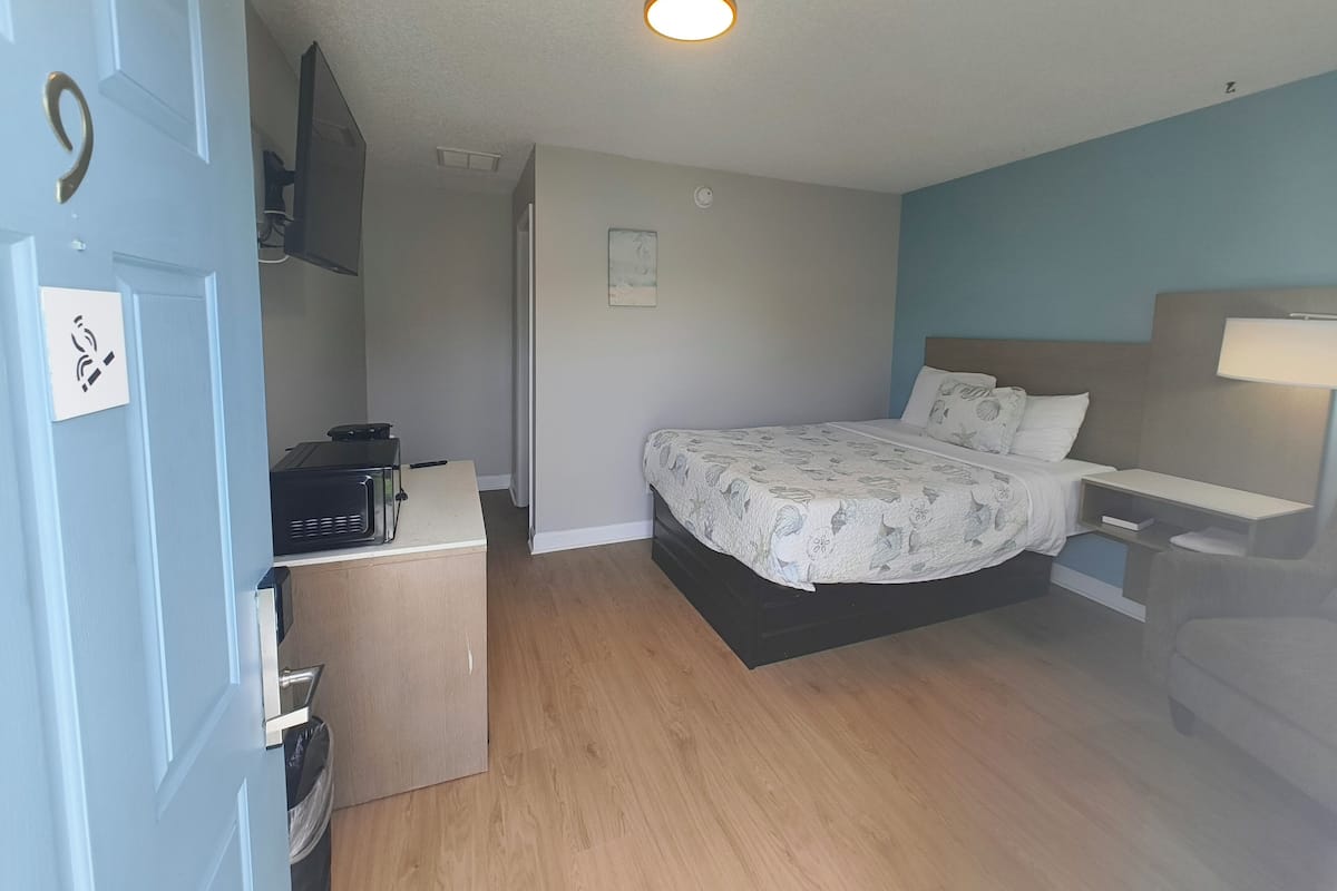 Un dormitorio con cama, mesita de noche y escritorio con computadora.