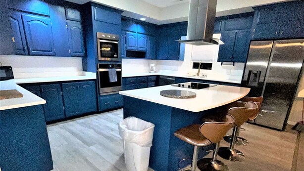 A modern kitchen with blue cabinets, stainless steel appliances, and a central island with bar stools. - Sand Dollar Motel (Atlantic Beach)