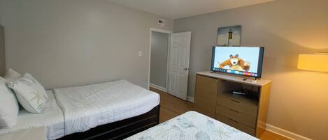 A bedroom with two beds, a television on a wooden dresser, and a door leading to another room.