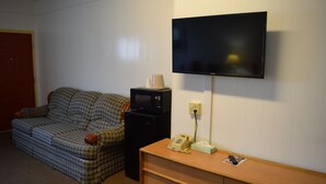 A room with a plaid sofa, a small black microwave, a wooden dresser, and a mounted television. - Economy Inn (Taylorville)