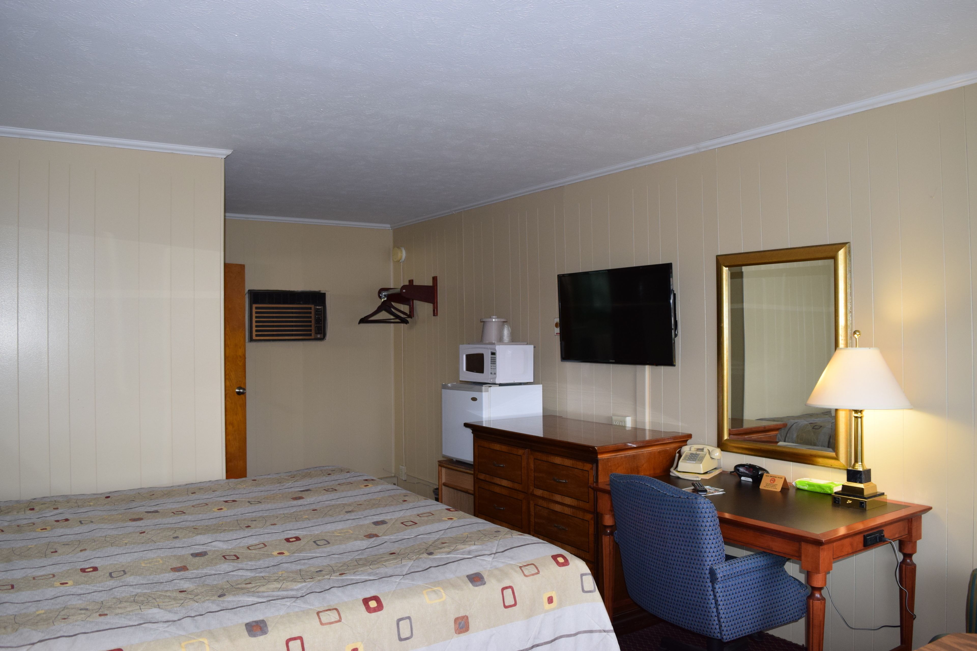 A hotel room with a bed, a desk with a lamp, a television, a microwave, and a mirror.