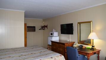 A hotel room with a bed, a desk with a lamp, a television, a microwave, and a mirror.