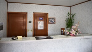 A reception desk with a wooden door, a sign indicating a smoking policy, a framed picture, and a potted plant. - Economy Inn (Taylorville)
