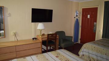 A hotel room with a bed, a desk with a chair, a television, and a red door.