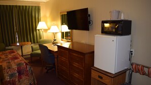 A hotel room with a bed, a desk, a chair, a television mounted on the wall, a microwave on top of a refrigerator, and a trash bin. - Economy Inn (Taylorville)