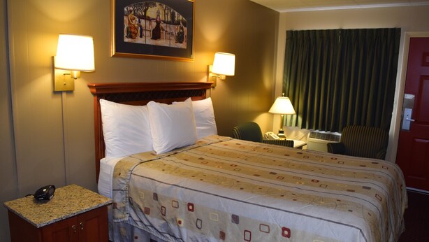 A hotel room with a large bed, two bedside lamps, a desk with a chair, a telephone, and a painting on the wall. - Economy Inn (Taylorville)