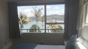 Una habitación de hotel con una cama grande, vista a un lago y un balcón con cortinas.