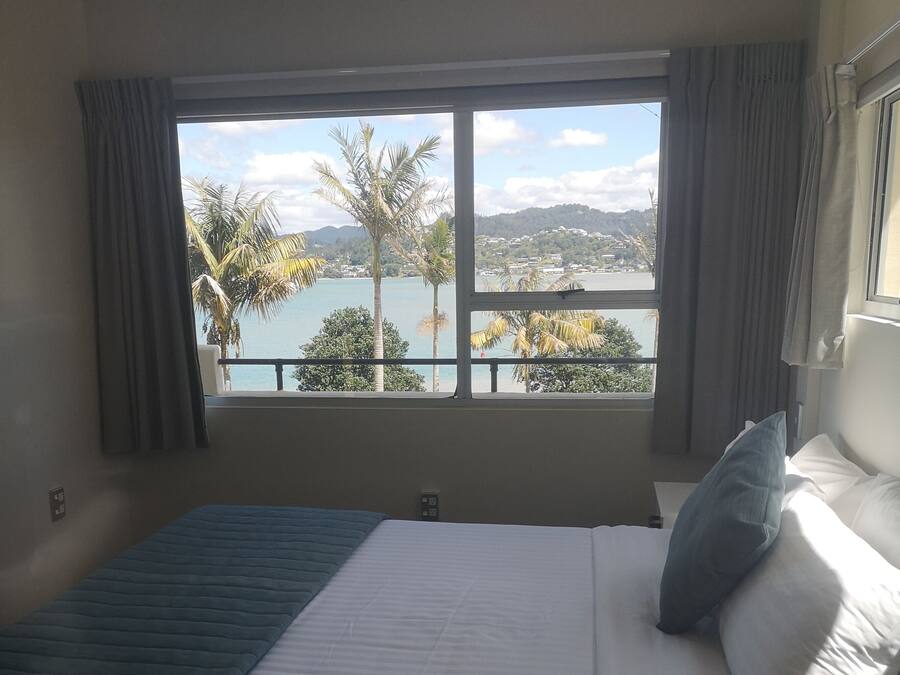 A hotel room with a large bed, a view of a lake, and a balcony with curtains.