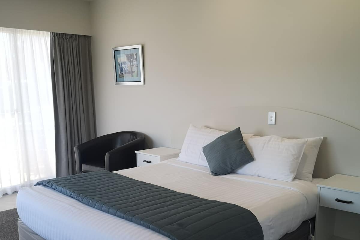 A modern hotel room with a large bed, a bedside table, a chair, and a window with curtains.