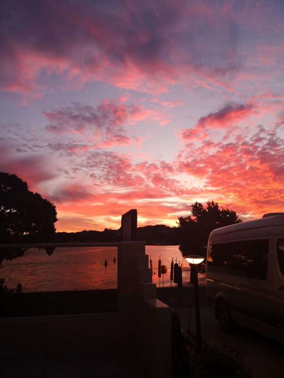 A sunset over a body of water with a van parked nearby.