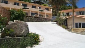 Un hotel de varios pisos con balcones, un muro de piedra de contención y jardines tropicales.