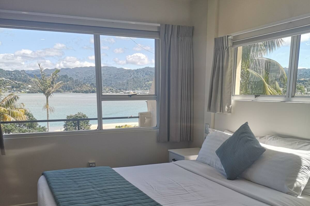 A hotel room with a large bed, a view of a lake, and a balcony.