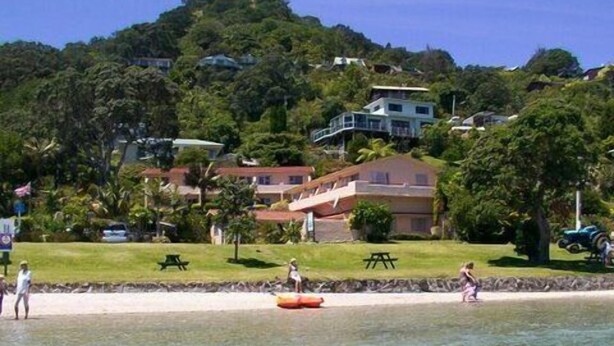 Zona costera con agua cristalina, una playa de arena y casas en una colina.