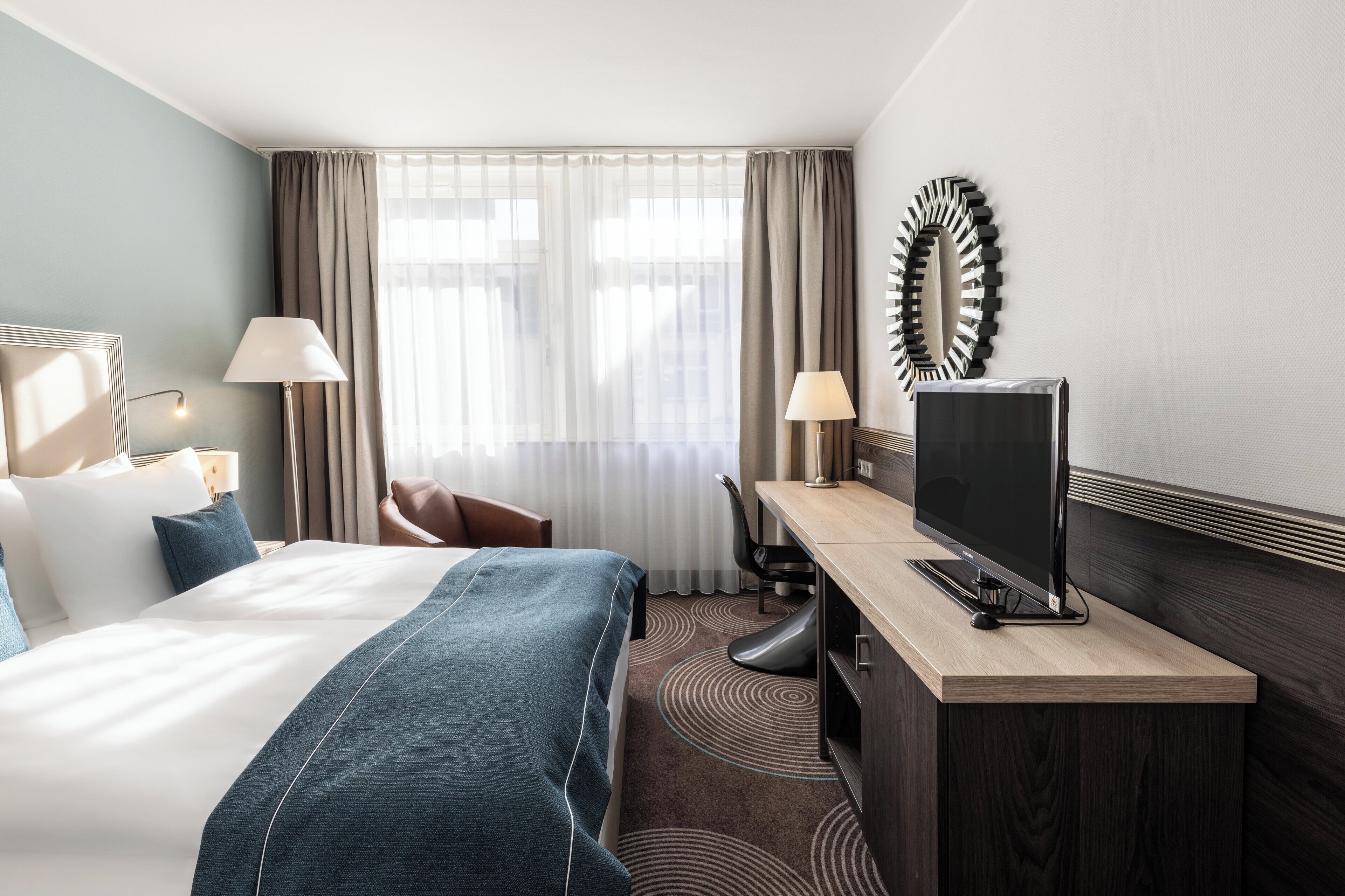 A hotel room with a bed, a desk, a TV, and a chair.