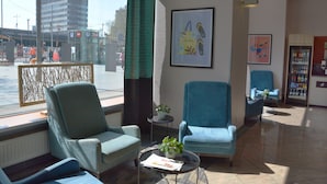 Un vestíbulo de hotel con dos sillones azules, una mesita con una planta y un cuadro en la pared.