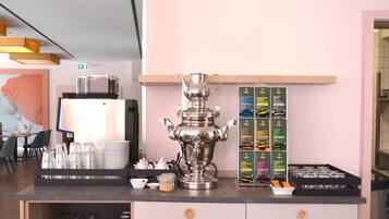 A kitchen counter with a large silver teapot, stacks of white plates, and a display of packaged food items.