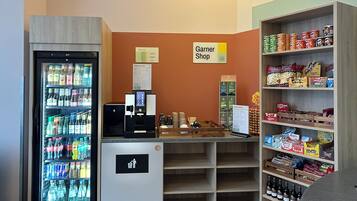 Area con distributori automatici per snack e bevande, una macchina del caffè, un cartello per 'Garner Shop' e scaffali pieni di snack e bevande.