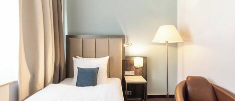 A hotel room with a bed, a nightstand, a lamp, a chair, and a patterned rug.
