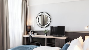 Habitación de hotel con cama, escritorio con computadora, televisor y espejo en la pared.