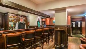 Zona de bar con taburetes de madera, un barman y una estantería bien surtida de licores.