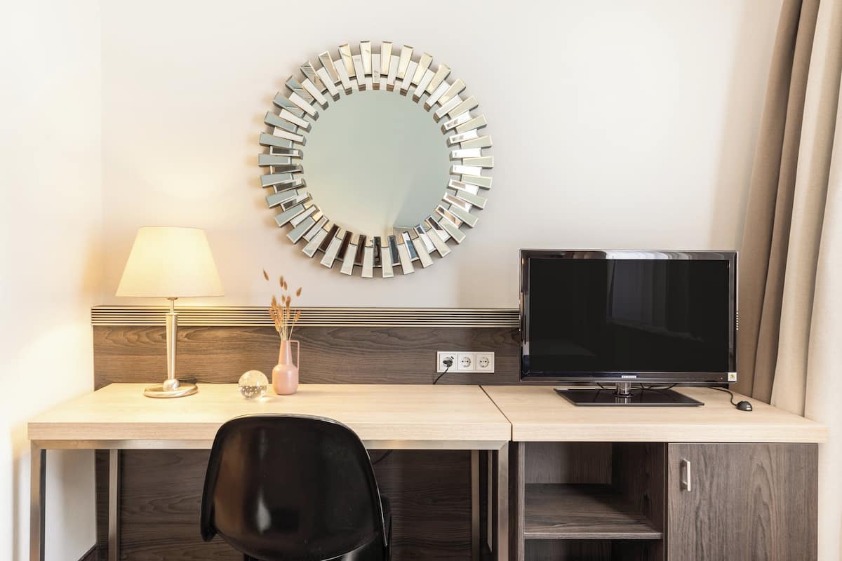 Een hotelkamer met een houten bureau, een zwarte stoel, een televisie, een lamp en een decoratieve spiegel.