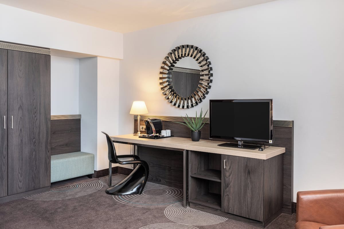 Een moderne hotelkamer met een bureau, stoel, televisie en een decoratieve spiegel.