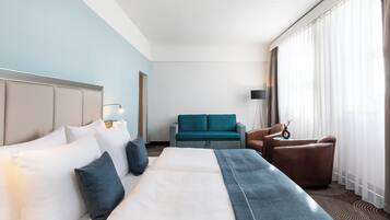 Una habitación de hotel con una cama, un sofá, una silla y una ventana con cortinas.