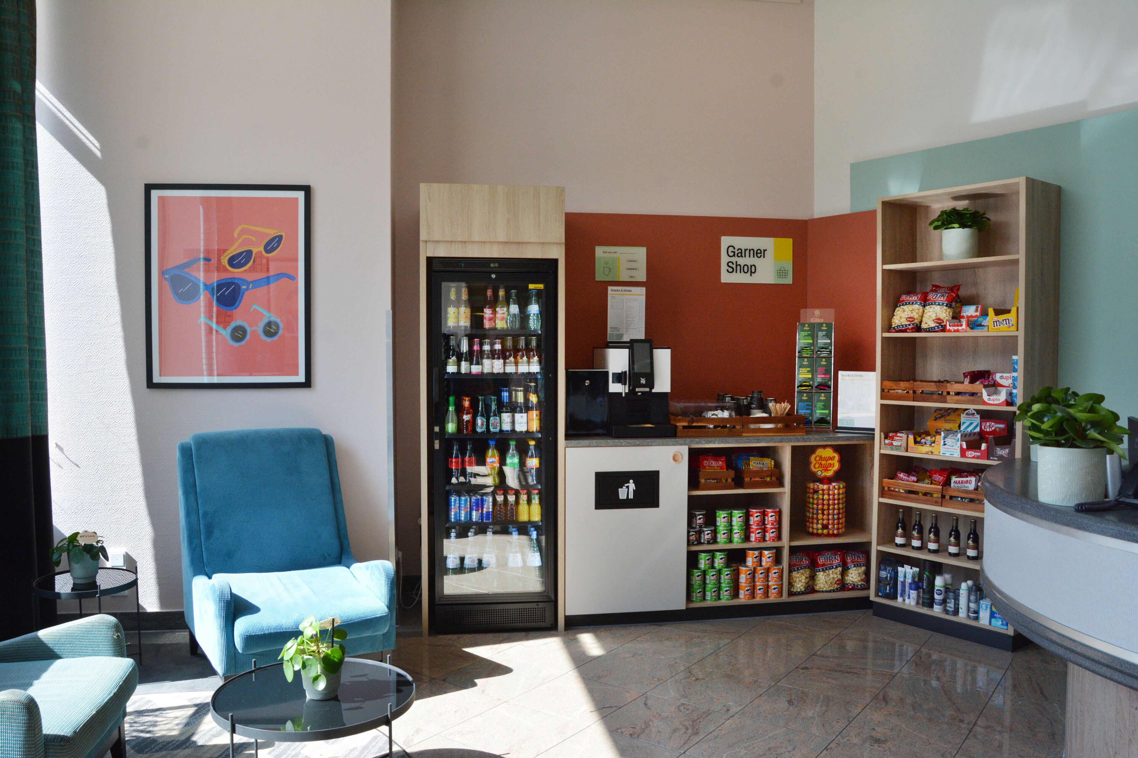 Un vestíbulo con un sillón azul, un refrigerador lleno de bebidas, un bar de aperitivos y un letrero para la tienda Garnier Shop.