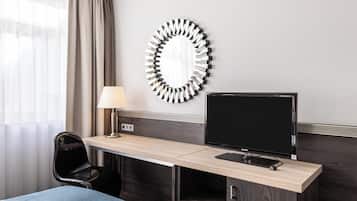 Habitación de hotel con escritorio, una silla, televisión, lámpara y un espejo grande en la pared.