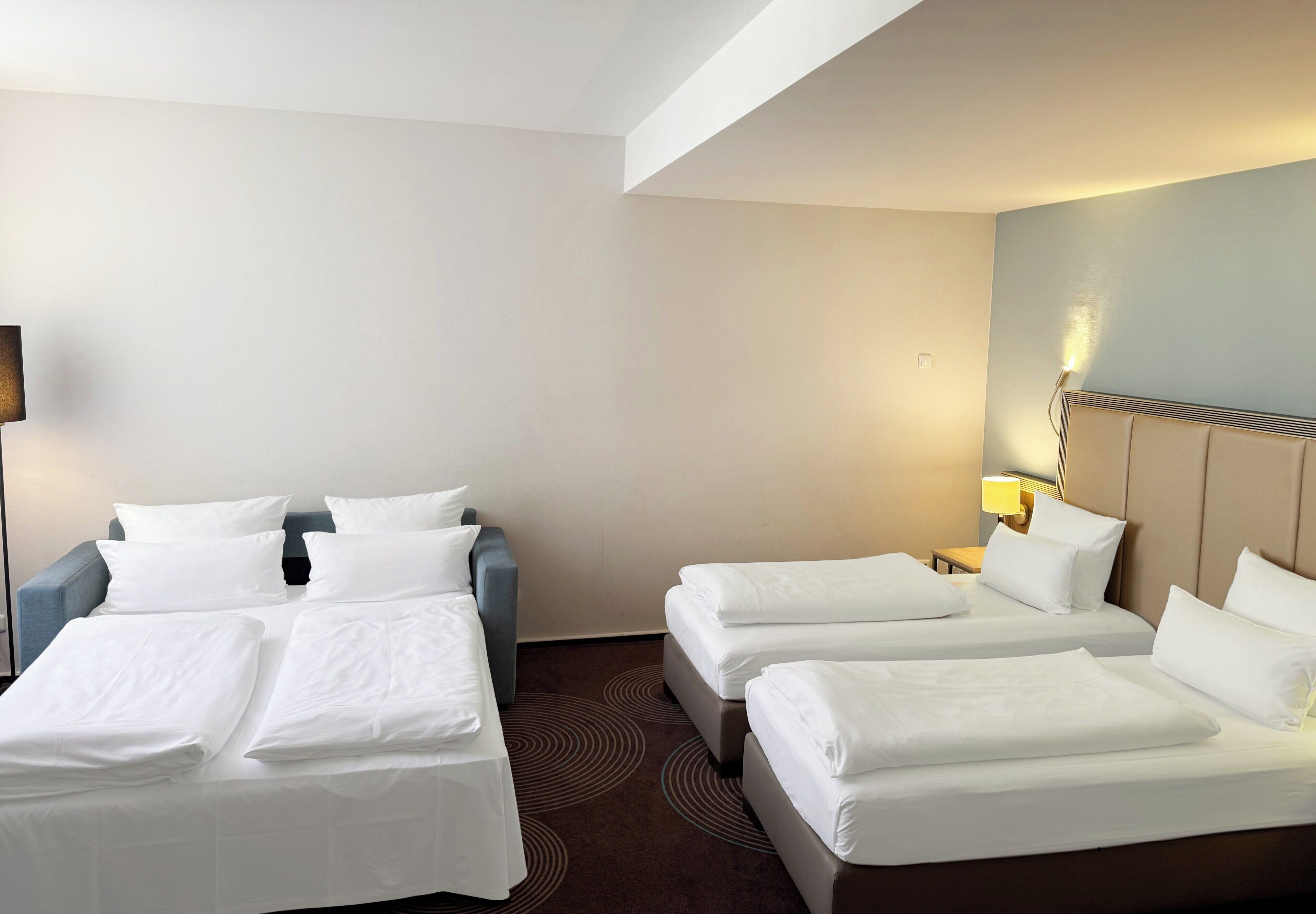 A hotel room with two single beds, a sofa, and a small table.