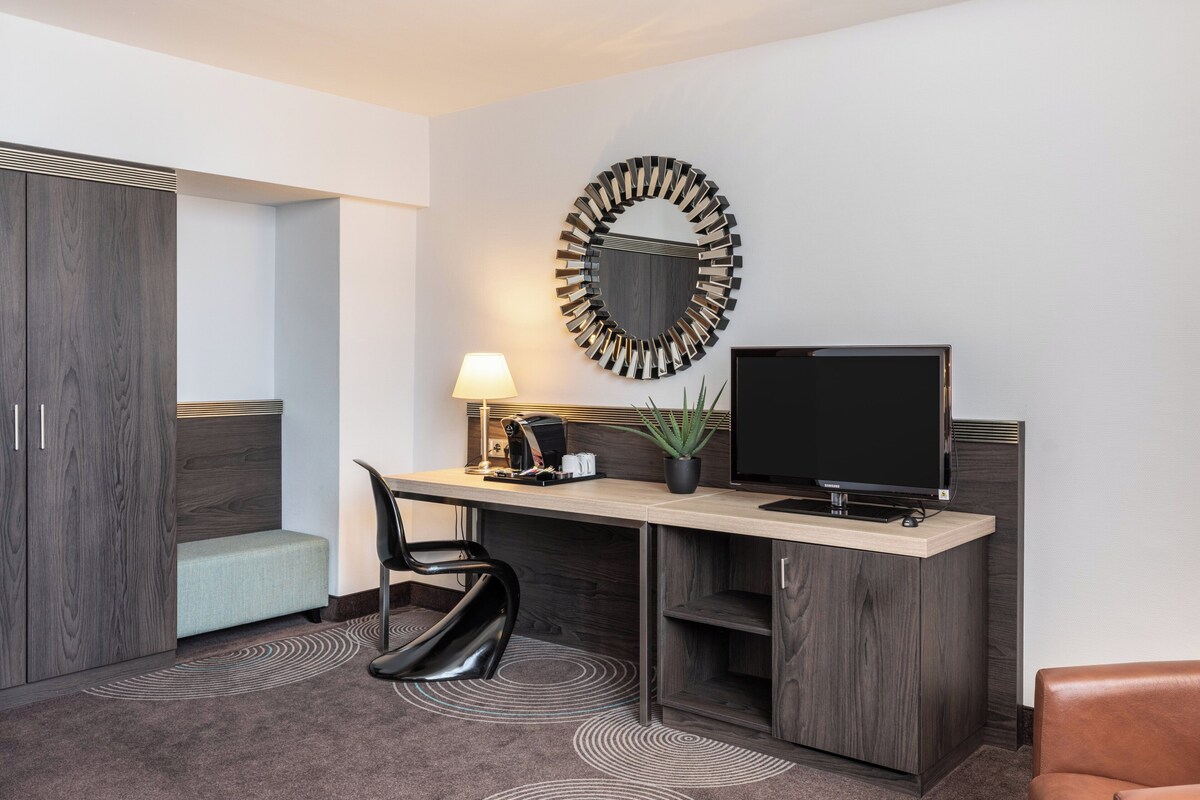 Ein modernes Hotelzimmer mit Schreibtisch, Stuhl, Fernseher und einem dekorativen Spiegel.