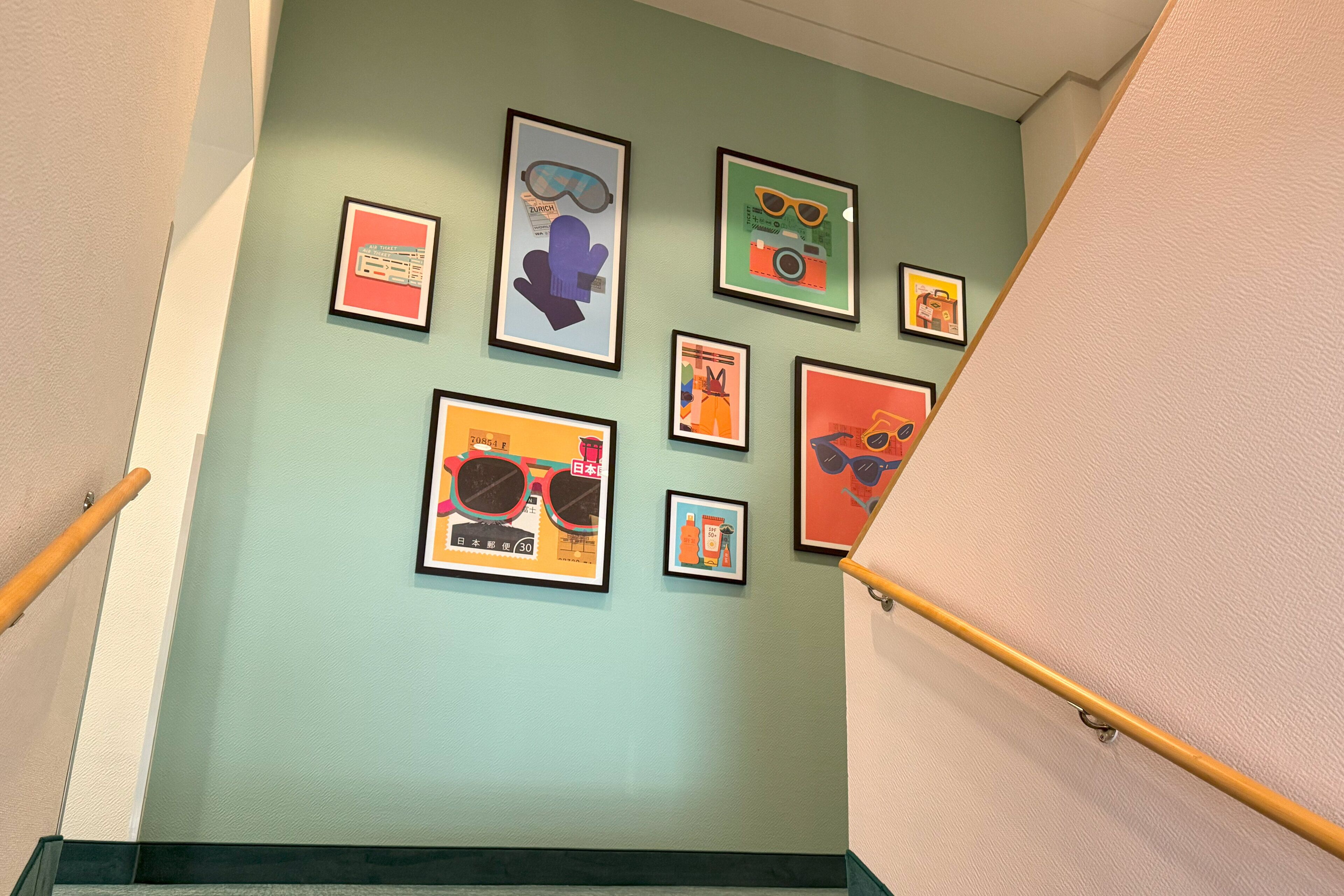 A staircase with a handrail, a green wall, and various framed artworks including sunglasses and a cat.