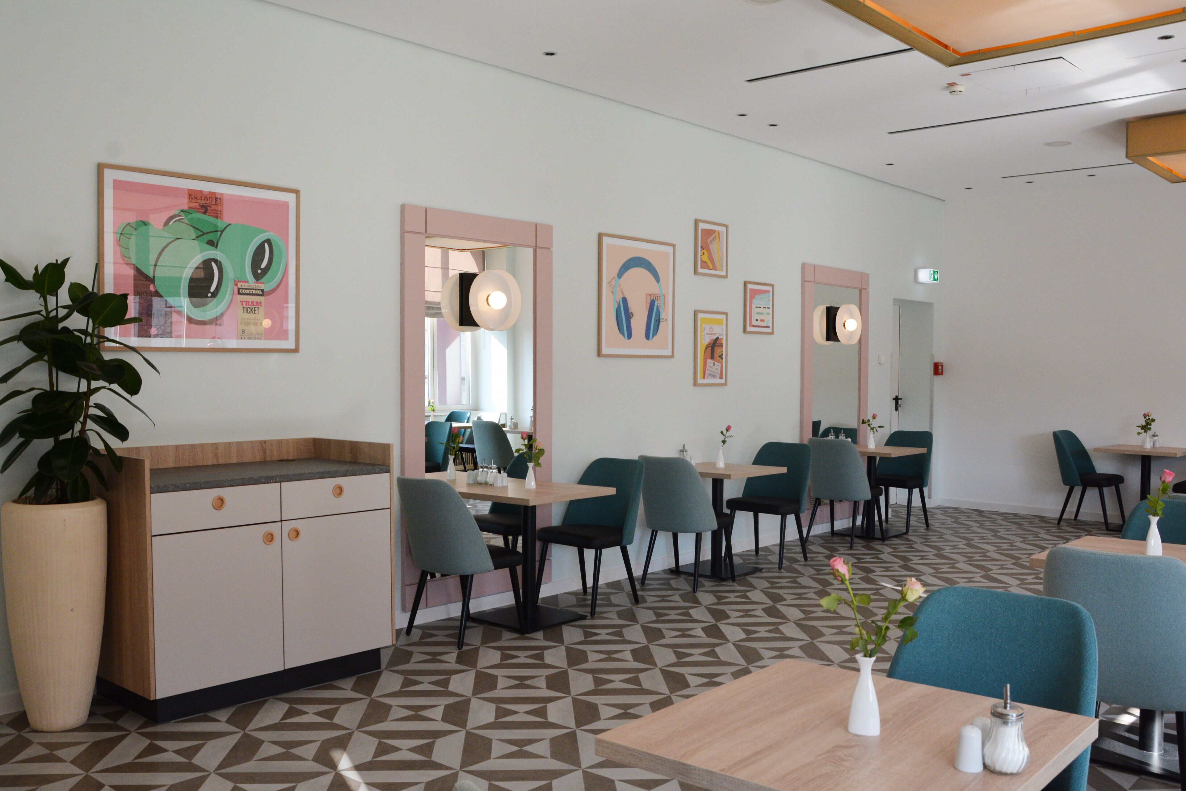 A modern restaurant with a geometric patterned floor, teal chairs, and wooden tables.