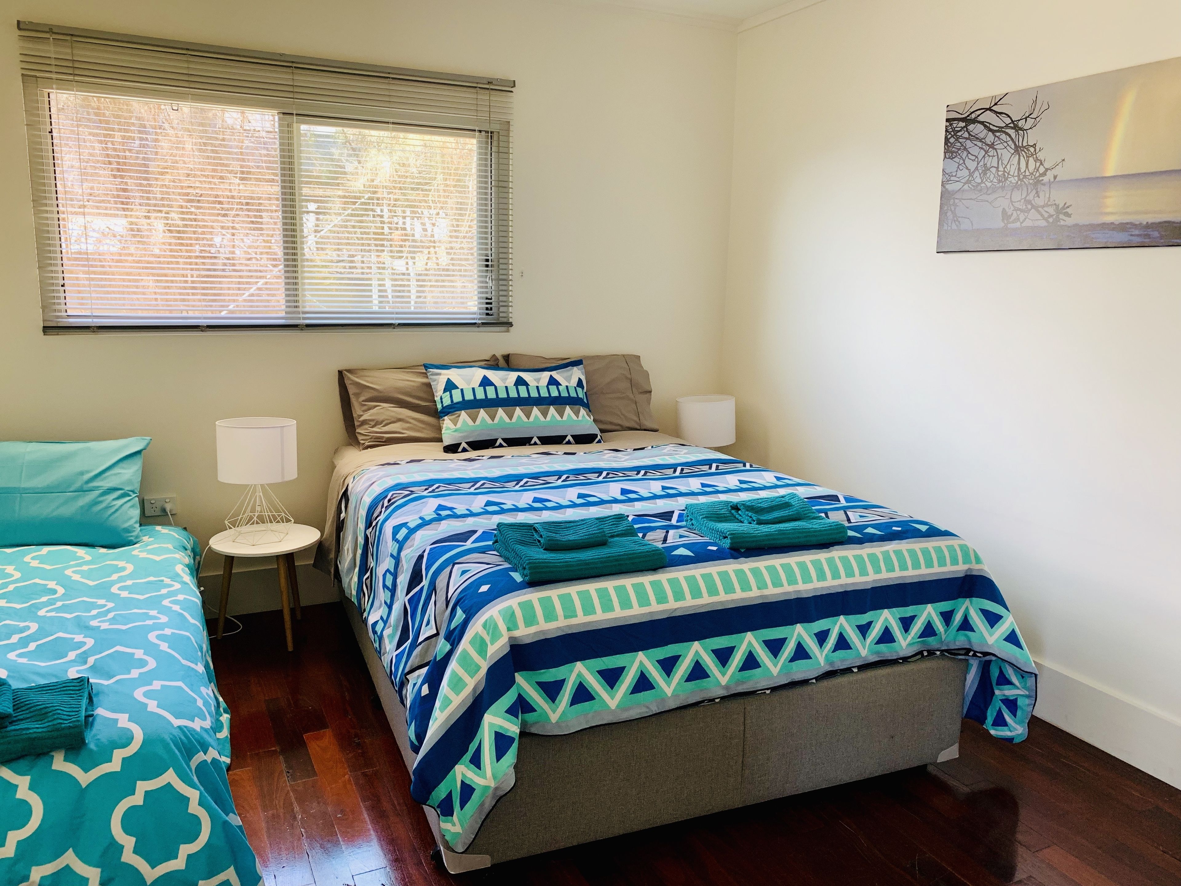 Een slaapkamer met een bed, twee nachtkastjes, een raam met zonwering en een aan de muur hangend kunstwerk.