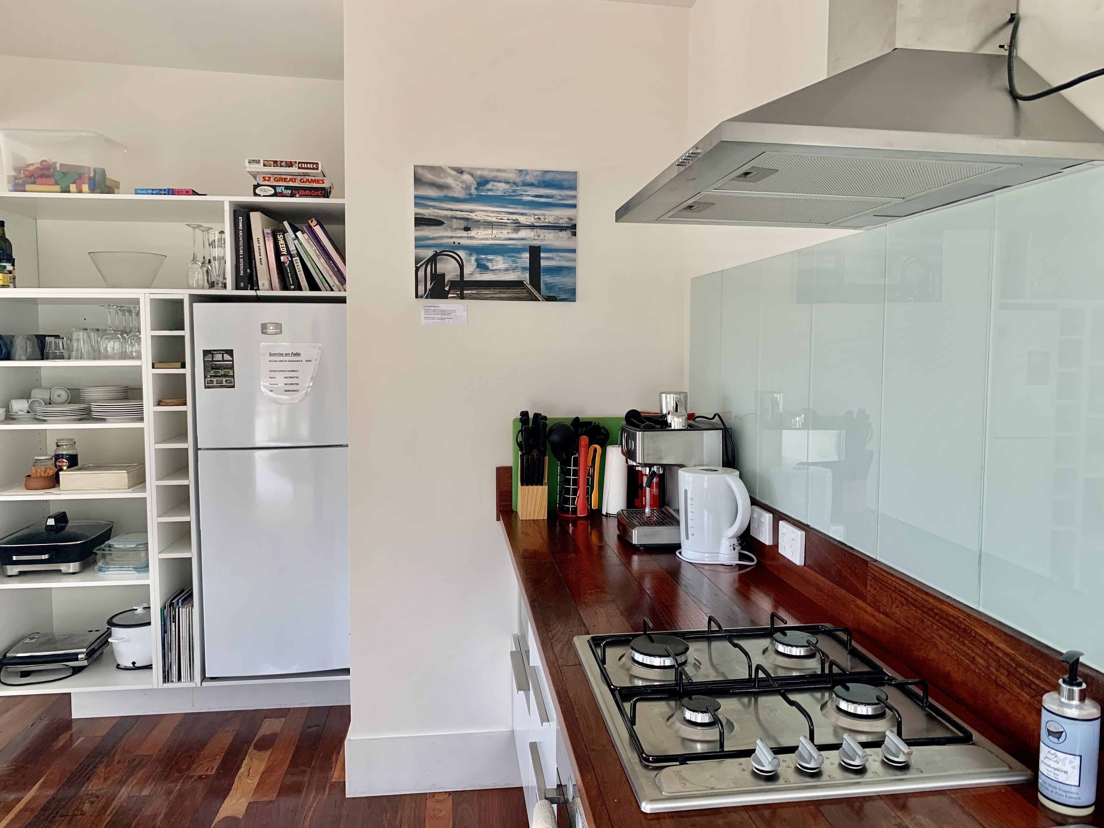 A kitchen with a white refrigerator, a gas stove, and a coffee machine. There are books and kitchen utensils on the counter.
