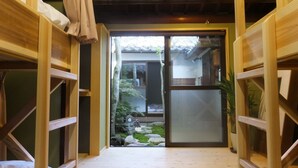Een traditionele Japanse kamer met tatami vloeren, houten stapelbedden en een glazen schuifdeur naar een tuin.