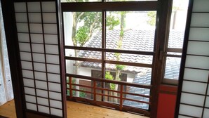 Een traditionele Japanse kamer met tatami vloerbedekking, een shoji schuifwand en uitzicht op een woonwijk met pannendaken.
