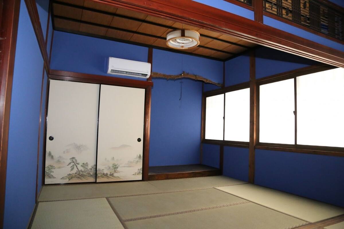 Een traditionele Japanse kamer met tatami vloeren, een schuifdeur met een natuurscène en een raam met uitzicht.