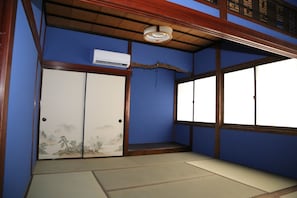 Una habitación japonesa tradicional con suelo de tatami, una puerta corredera con una escena de naturaleza y una ventana con vistas.