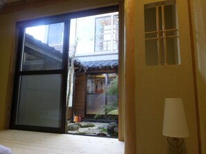 A traditional Japanese room with tatami flooring, a sliding door, and a view of a garden with rocks and plants.