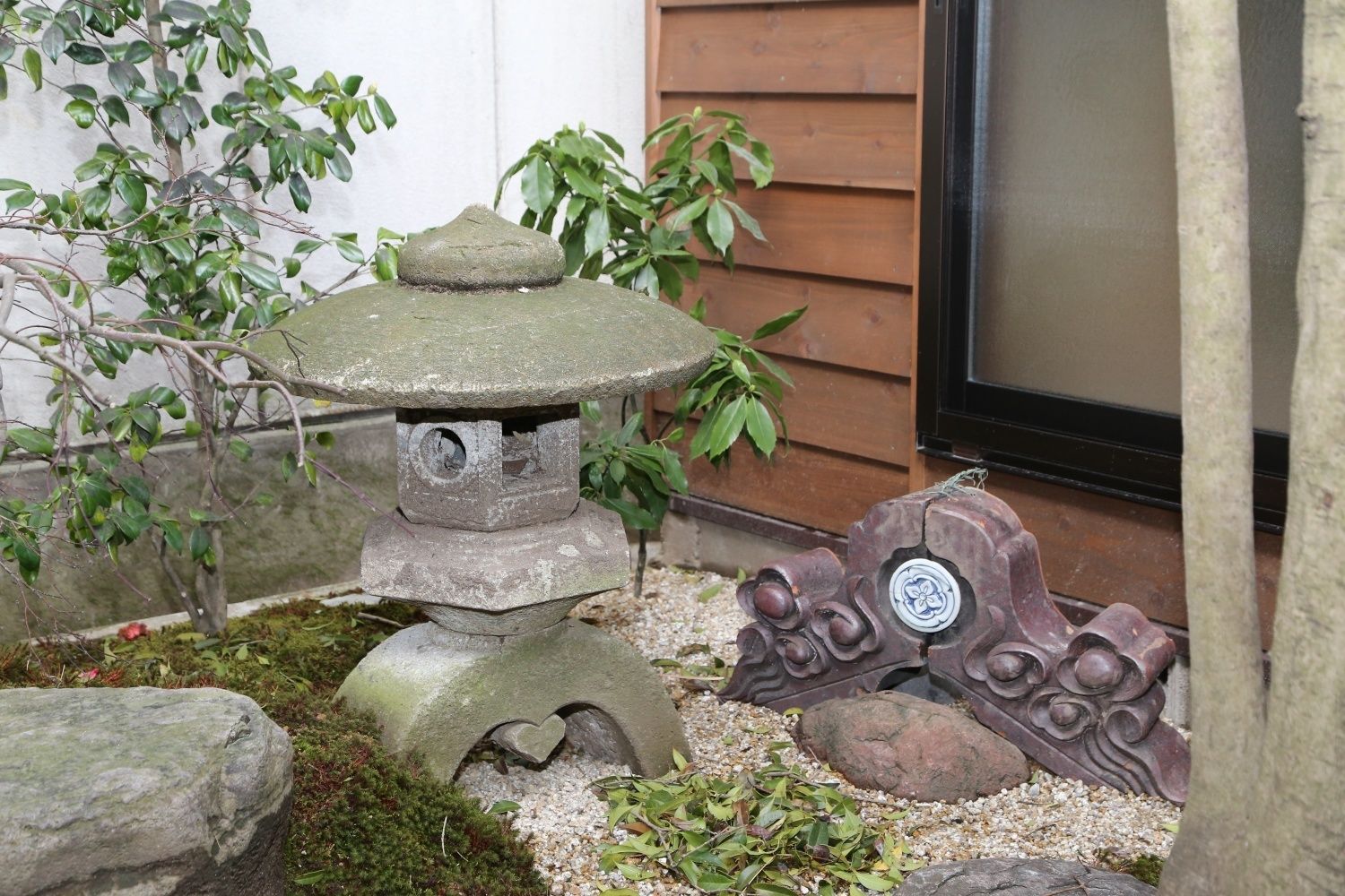 A stone lantern with a heart-shaped base, surrounded by rocks and moss, in a garden setting.