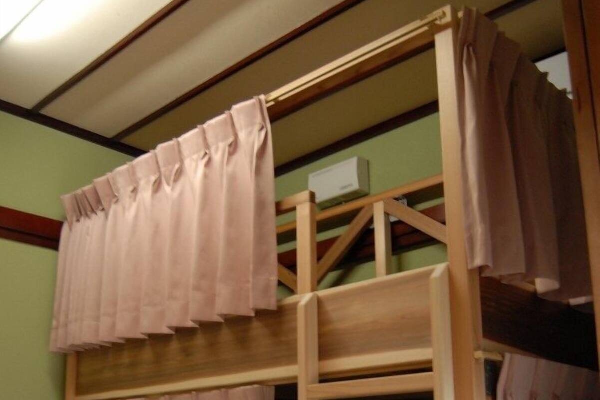 Een stapelbed met roze gordijnen, een houten frame en een klein bureau.